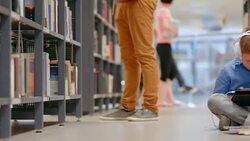 DS Boy sitting on library aisle browsing on tablet Stock Footage