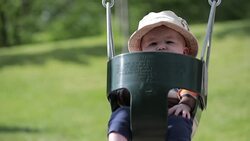 Happy Baby Boy Sitting in Playground Swing Outdoors with Mom Stock Footage