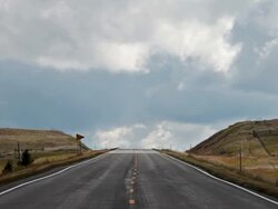 WS T/L View of Telephoto shot of road going over hill with dramatic clouds boiling in sky / White Sulphur Springs, Montana, United States Stock Footage