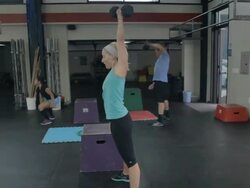 Profile angle, camera tracks in on Carly as she performs dumbell snatches; Jonice and Steven perform dumbell snatches in background. Stock Footage