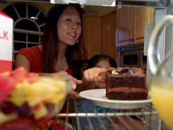 Refrigerator point of view Asian woman taking bowl of fruit from shelf and showing to young girl Stock Footage