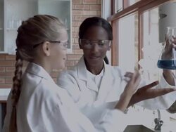 MS Two school girls looking together at blue liquid in beacon Stock Footage