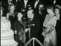 First Lady Eleanor Roosevelt, James Cagney, Edgar Bergen, Charlie McCarthy and others blow out candles on a large cake. News Clip