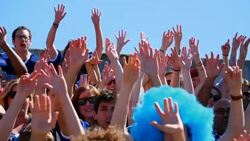 MS Crowd of fans in stadium waving hands in air and standing up in unison to cheer during football game Stock Footage