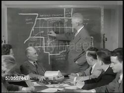 1950: SCHOOL REFORM: Sign: Senate Committee on Education. REPRISING MEETING: Male at board talking about district divisions. Newspaper Headline 'Legislature Approves Unit District Bill'. COUNTRY ROAD: Sedan automobile driving on two-lane country road. Instructional Video