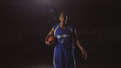 A male basketball player dribbles a ball at center court and then holds the ball while looking serious. Stock Footage