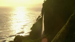 Waves lap the shore as a waterfall pours from a cliff on Hawaii's Hamakua Coast. Stock Footage