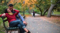 New York couple in love nuzzle on park-bench in Central Park, boyfriend kisses girl on cheek sweetly (dolly-shot) Stock Footage