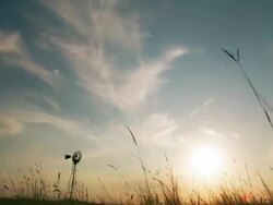 Timelapse of clouds over a windmill at sunset with tall grass in the foreground Stock Footage
