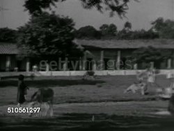 1966: ITA, PARAGUAY: Angled MS (POV moving vehicle) passing two men on horseback, 'Ita' roadside sign, WS PAN People in compound courtyard lined w/ buildings, VS Native peoples, non-native brunette woman getting off donkey w/ saddlebags. Instructional Video