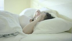 Beautiful young woman waking up in bed smiling, yawning, and stretching Stock Footage