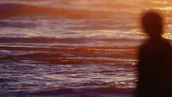 The evening sun lights up the ocean like fireworks on the 4th of July. A person silhouetted against the light walks through the frame. Stock Footage