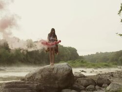 Woman on big rock in nature with red smoke around her Stock Footage