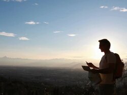 Man walks above city into rising sun, checks map and GPS Stock Footage