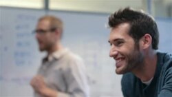 Older businessman types on smart-phone; positive young businessmen lead meeting in office conference-room Stock Footage