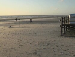 WS View of people walking on sea coast and sea sand flying by wind during sunset, North Sea North Frisia, / St. Peter Ording, Schleswig Holstein, Germany Stock Footage