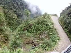 A Bolivian bus drives along a treacherous mountain dirt track as fog fills the valley below.. Stock Footage