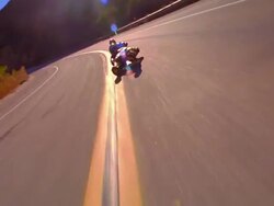 CANTED tracking shot two street lugers speeding past camera on mountain road / sun flare in shot Stock Footage