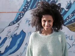 Young woman with curly hair looking into camera, smiling, laughing in sunshine Stock Footage