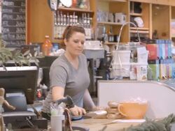 female coffee house employee removes sugar coated cookie from bakery display case with pastry tong and places cookie onto napkin on counter / Redlands, California, USA Stock Footage