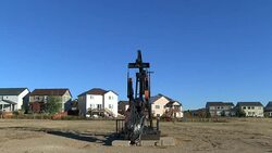 Oil well pump jack just outside the backyards of homes in Frederick, Colorado Stock Footage