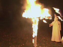 RECREATION Wooden cross is engulfed in flames as KKK members in white robes are standing in a semi-circle around it / Rockford, Illinois, United States Stock Footage