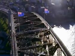 Aerial over the top of Sydney Harbour Bridge, flags, Sydney Opera House, Australia Stock Footage