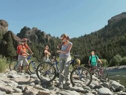 People with mountain bikes by lake, woman taking a photograph Stock Footage