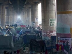 Kumbh Mela camp set up under motorway flyover, makeshift tents, washing lines, cooking, men, women, children.  India Stock Footage