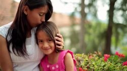 Older sister kisses young hispanic girl's head and smiles at camera Stock Footage