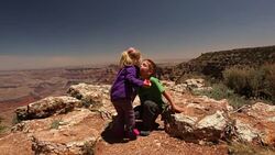 Sister gives her brother a kiss while enjoying an apple on the rim of the Grand Canyon Stock Footage