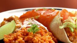 wet burrito on a plate with brown rice and beans as diced green onions are sprinkled over burrito Stock Footage