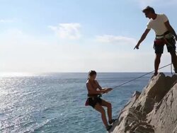 Father lowers daughter to base of rock climb above sea Stock Footage