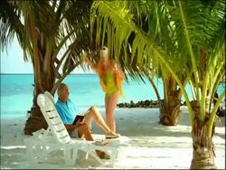 MS elderly man sitting on sun longer joined by elderly woman with drinks Stock Footage
