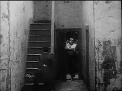 B/W 1917 large man (Eric Campbell) chasing policeman Charlie Chaplin upstairs in building Stock Footage