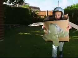REAR POV Girl running in yard inside cardboard airplane / Great Yarmouth, England, United Kingdom Stock Footage