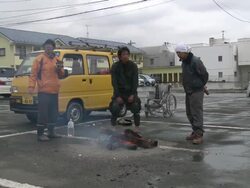 Destruction caused by tsunami after magnitude 9 Tohoku earthquake, north east Japan, March 2011. Men stand around fire in car park after tsunami in Ishinomaki, Miyagi Prefecture Stock Footage