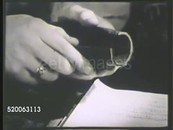 1935: MOTOR HOSE TESTING: MS Engineer sitting at table cutting open motor hose connection. MCU Inner wall of hose revealing decay & rot, male hands running through decay. WS Another male engineer taking notes by test wall of hoses. Antifreeze Instructional Video