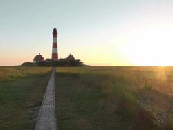 WS View of Westerhever lighthouse with walking trails from grass field at sunset, North Frisian Wadden Sea / Westerhever, Schleswig Holstein, Germany Stock Footage