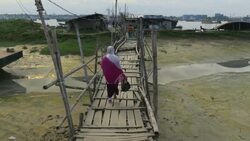 A woman crosses a rickety wooden bridge on a riverbank to access traditional ferry boats in Chittagong Bangladesh  Stock Footage