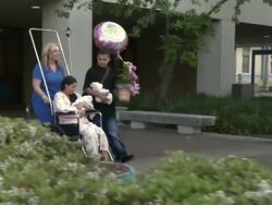 Nurse pushing a mother holding her newborn baby in a wheelchair leaving the hospital Stock Footage