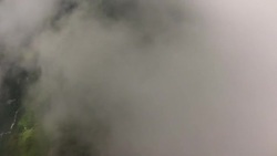 POV wingsuit flying through dense clouds and breaking through to fly over green cliffs and forest Stock Footage