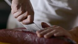 Restaurant chef cuts thick slab of tuna steak on chopping block in restaurant kitchen Stock Footage