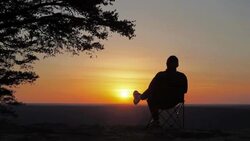 Silhouette of Single Man Sitting in Chair Relaxing at Sunset on Summit Stock Footage