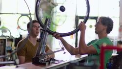 Bike shop customer brings bicycle wheel for mechanic to put on truing stand and spin Stock Footage