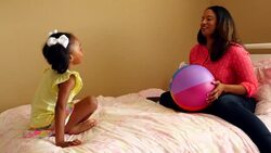 MS ZI Smiling mother and daughter sitting on bed throwing ball back and forth Stock Footage