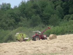 WS Bale of straw and tractor with baling press in grass field / Serrig, Rhineland-Palatinate, Germany Stock Footage