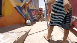 Young Brazilian boys pass soccer ball down alleyway tagged with colorful graffiti and kick ball at camera in slow motion Stock Footage