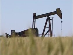 MCU Low angle view ripening wheat field foreground waving in wind, pull focus to oil pump operating on horizon, pull focus to crop foreground, USA Stock Footage