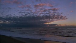 Clouds glow above waves washing into shore. Stock Footage